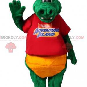 Zelený maskot dinosaura s červeným tričkem a žlutými šortkami -
