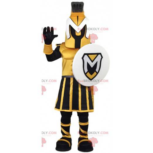 Mascota guerrera amarilla y negra con un escudo. -