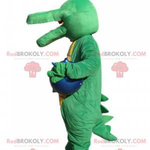 Green crocodile mascot with a blue balloon. - Redbrokoly.com