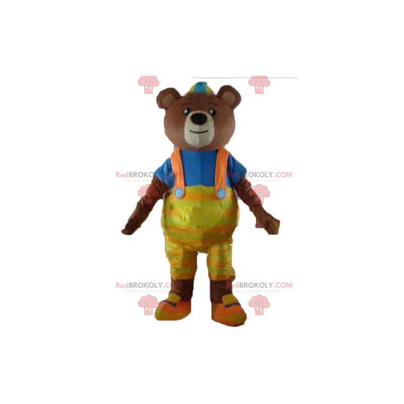 Brun björnmaskot med gula overaller och en t-shirt -