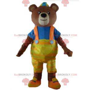 Mascotte orso bruno con tuta gialla e una maglietta -
