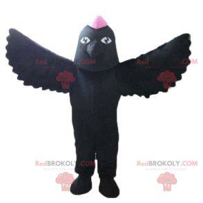 Schwarzes Vogelmaskottchen mit einem rosa Wappen auf dem Kopf -