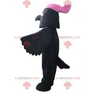 Schwarzes Vogelmaskottchen mit einem rosa Wappen auf dem Kopf -