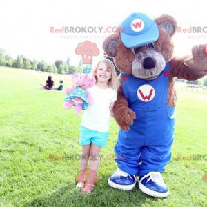 Mascotte de nounours marron avec une salopette bleue -