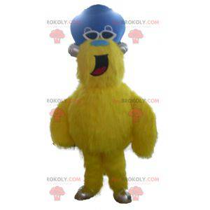 Mascote monstro amarelo e peludo com chapéu - Redbrokoly.com