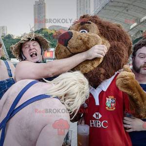 Mascotte de lion marron tout poilu en tenue de sport rouge -