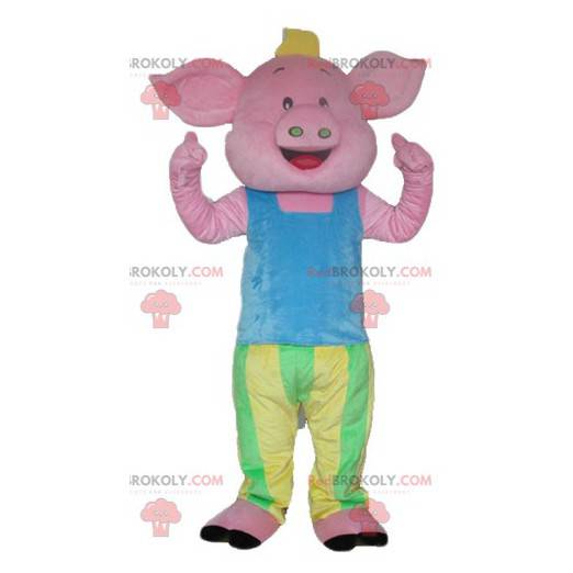 Różowa maskotka świnia w niebieskim, zielonym i żółtym stroju -