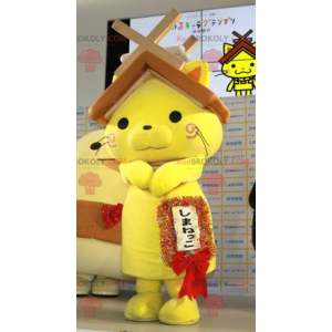Gelbes Katzenmaskottchen mit einem Hausdach auf dem Kopf
