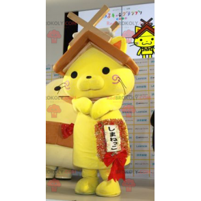 Gelbes Katzenmaskottchen mit einem Hausdach auf dem Kopf -