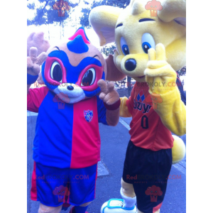 2 mascotte: un orso giallo e un animale mascherato blu e rosso