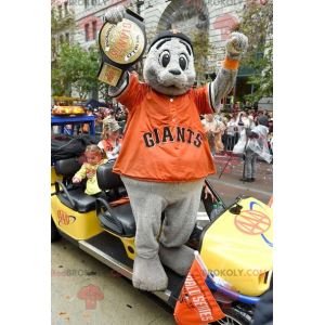 Mascote leão marinho cinza com uma camiseta laranja -