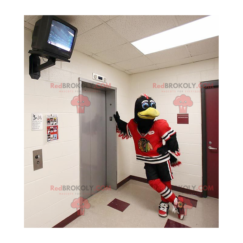 Mascotte d'oiseau noir et blanc avec une tenue de sport rouge -