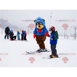 Braunes und gelbes Bärenmaskottchen im Ski-Outfit. Winter