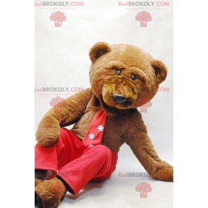 Maskotka niedźwiedź brunatny z krawatem i czerwonymi spodniami