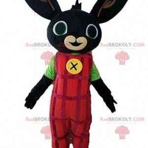 Černý králík maskot oblečený v červených montérkách -