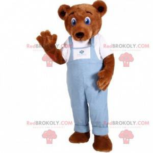 Mascotte bruine teddy gekleed in een overall van spijkerstof -